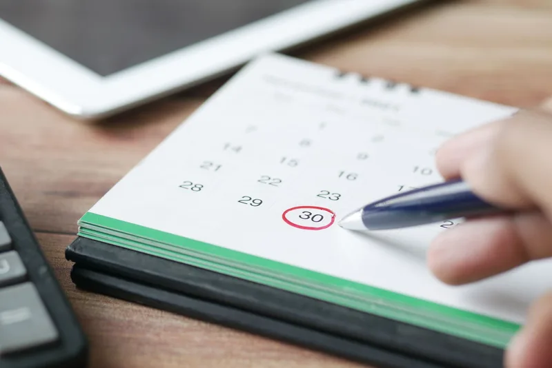 Hand marking a date on a calendar to schedule a review