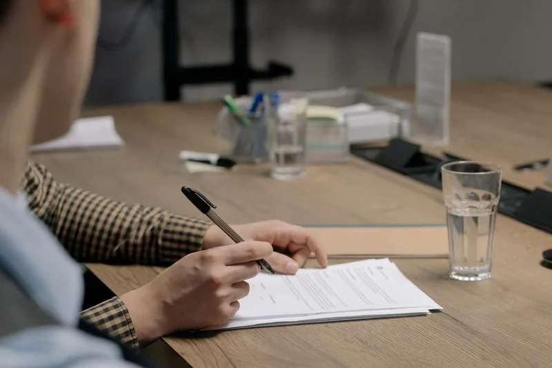 Close-up of a person signing and writing on a printed document at a desk